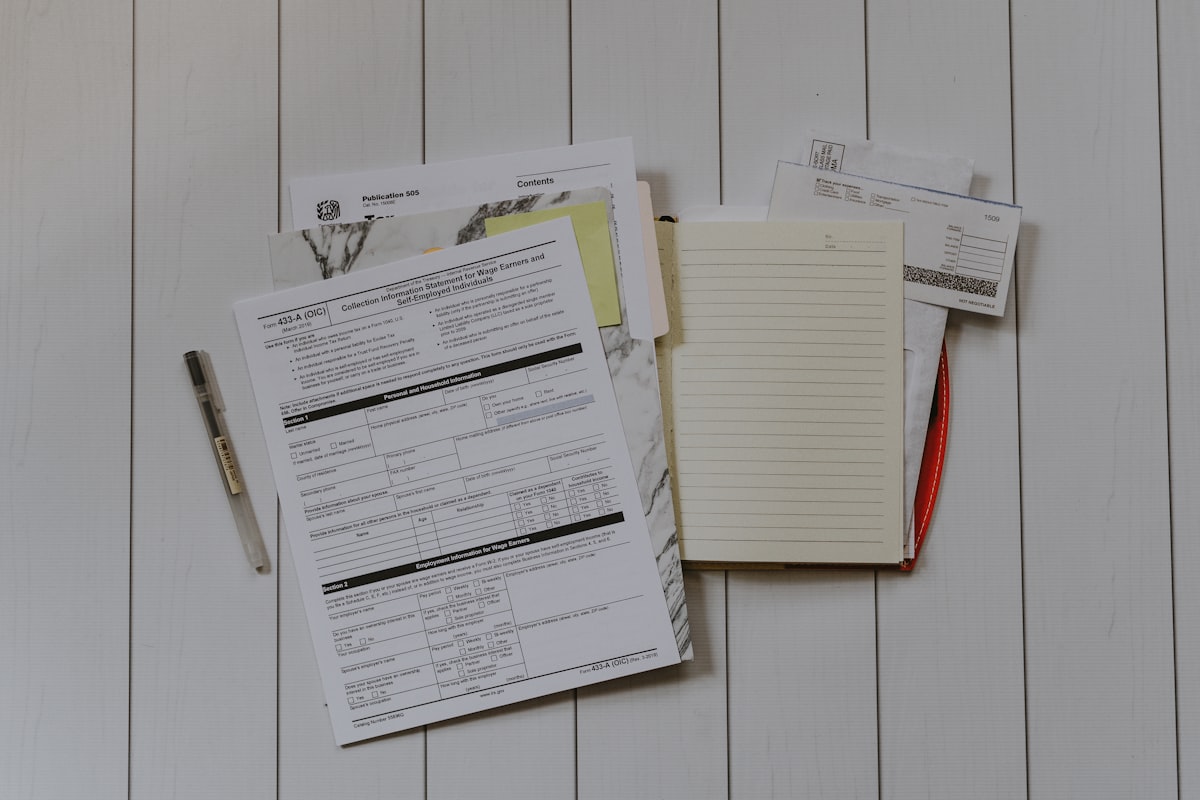 Stack of accounts-payable forms and paperwork spread across a desk with a pen