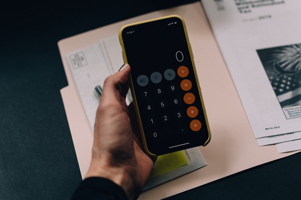 A hand holding a calculator over financial statements and spreadsheets on a desk