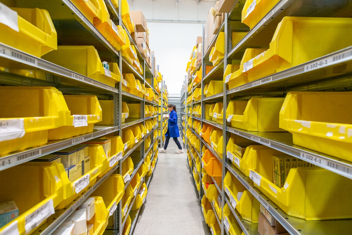 Warehouse picking aisle lined with labeled yellow small-parts bins on tall shelving