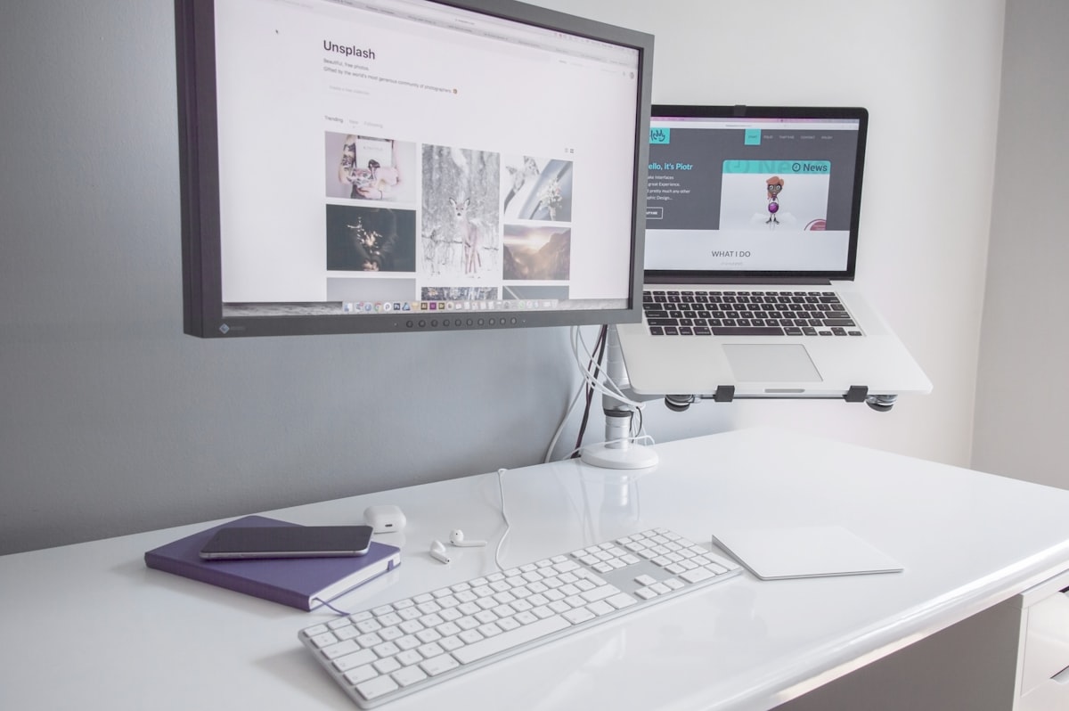 A clean white desk with a fresh laptop, external monitor, keyboard and notebook set up for a new employee