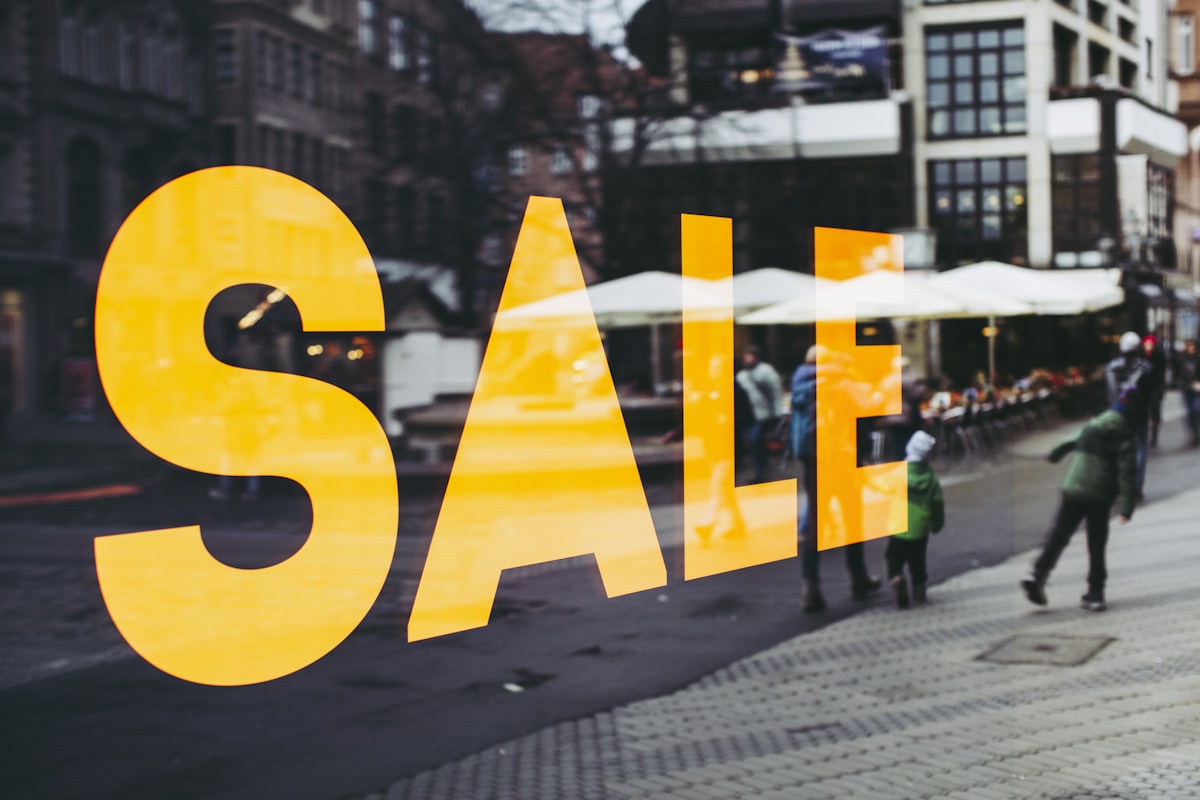 A large yellow SALE sign in a shop window overlooking a busy street
