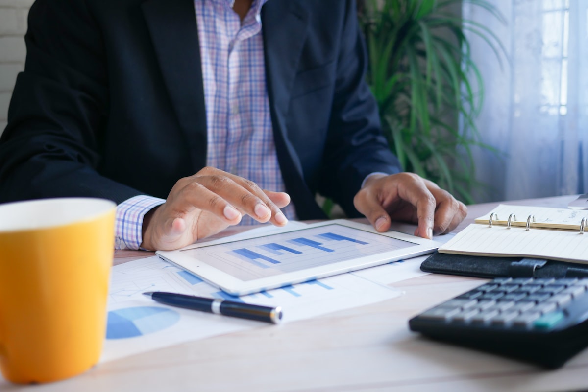 Finance professional at a desk reviewing printed financial records with a calculator and tablet
