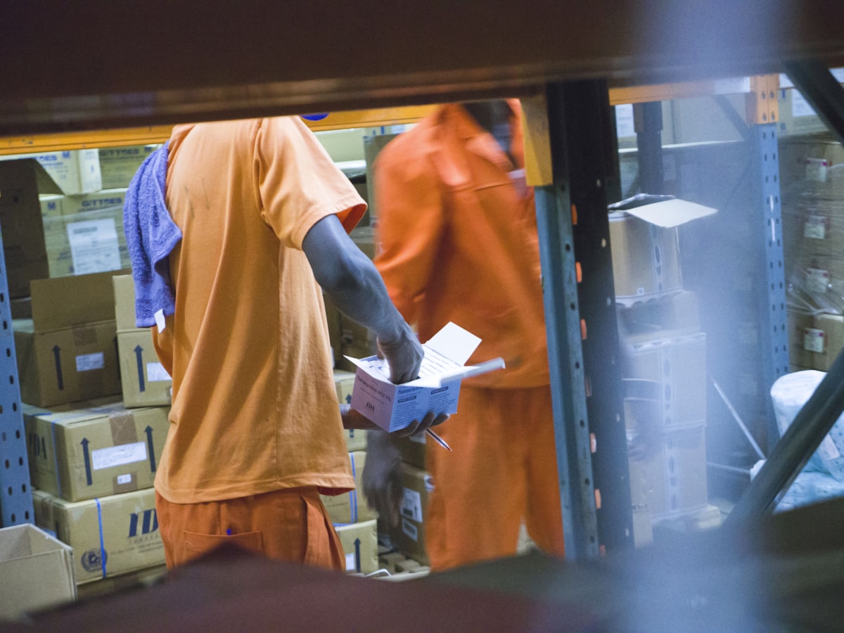Warehouse worker checking a product carton against paperwork beside racked inventory