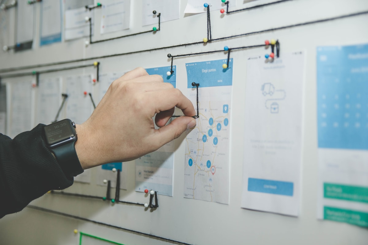 A hand pinning a printed note onto a planning board where papers are connected by string