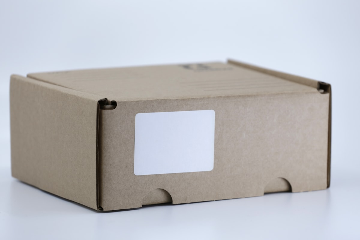 A brown cardboard shipping box with a blank white shipping label on a clean surface