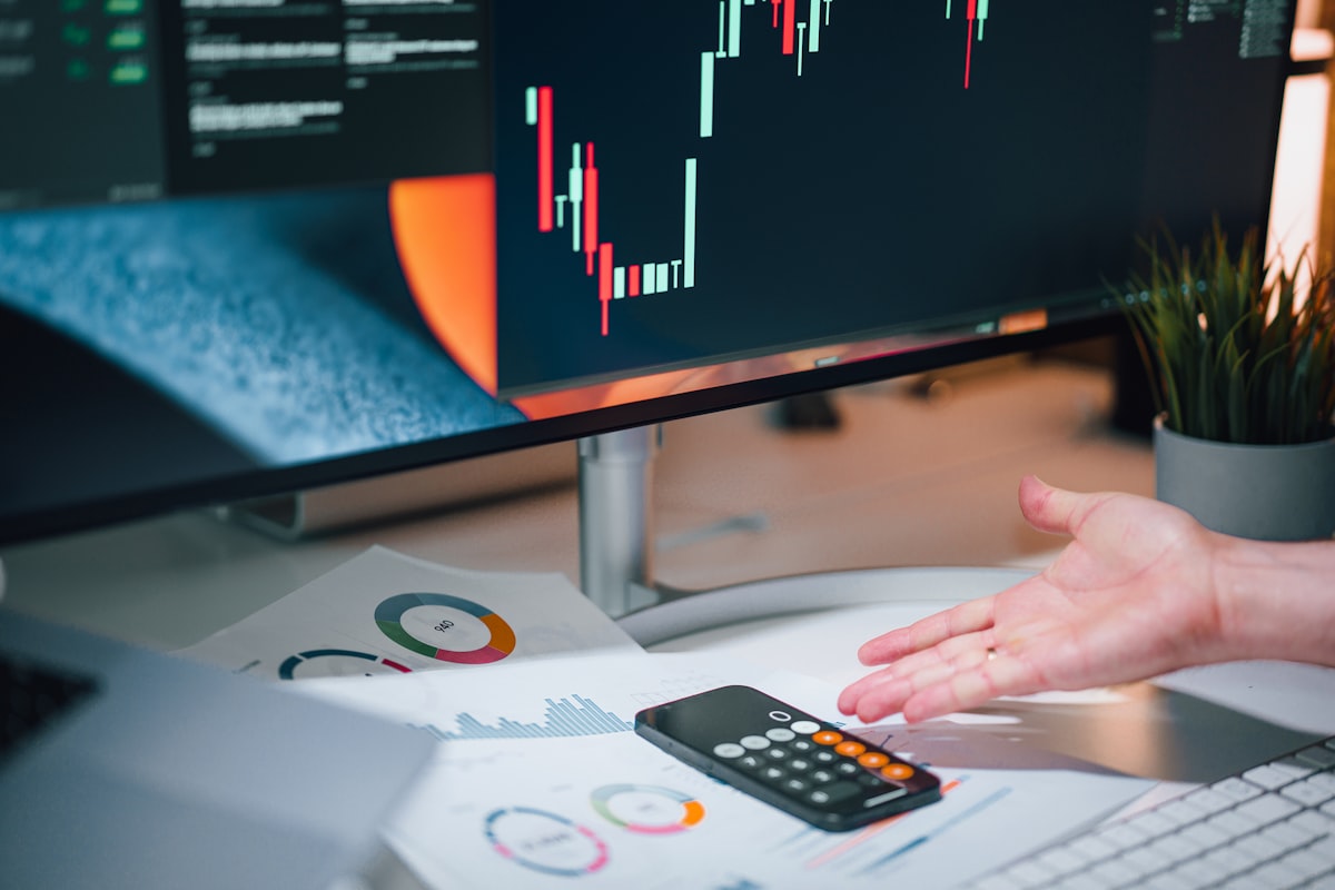Analyst at a desk reviewing financial charts on a computer monitor alongside printed graphs