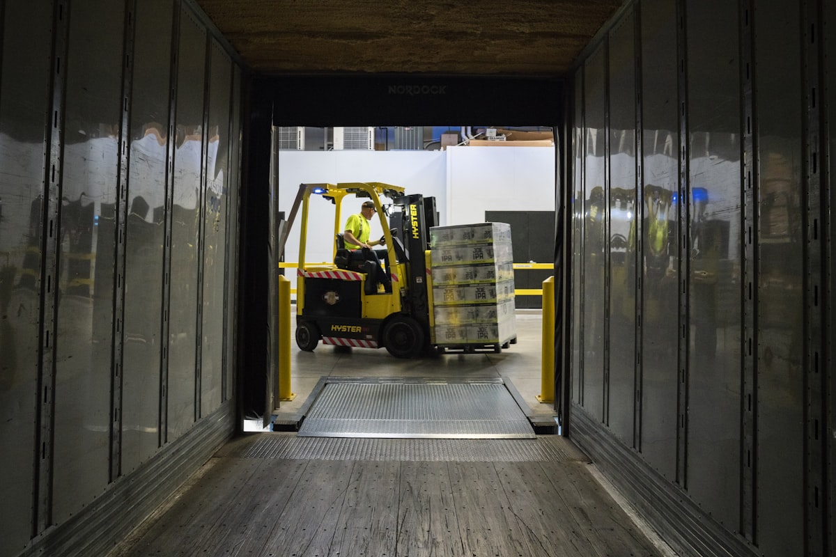 Forklift receiving a pallet of goods at a warehouse loading dock viewed from inside the trailer