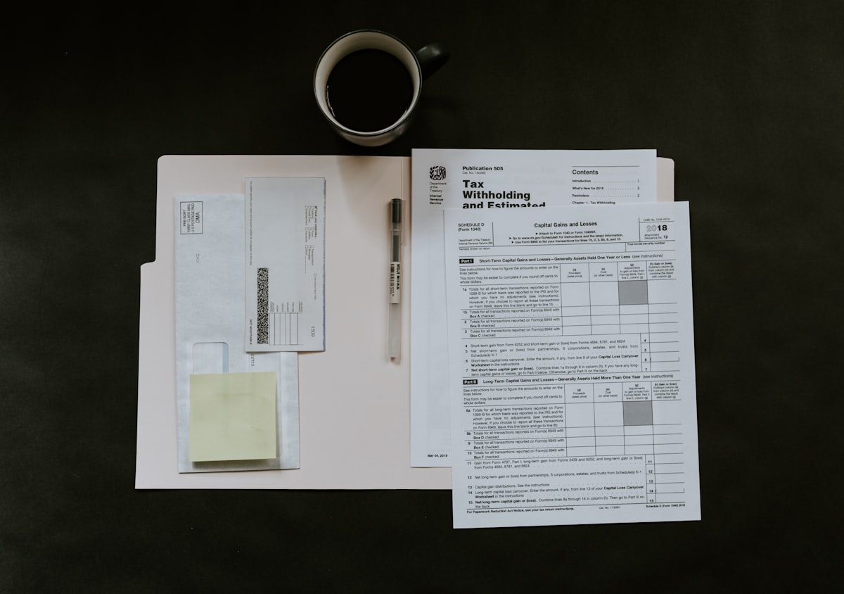 Printed financial documents laid out side by side on a desk for cross-checking, with a pen and coffee